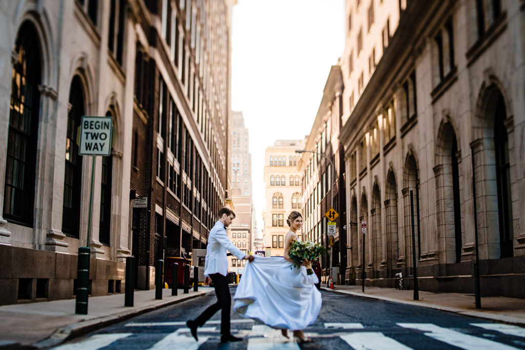 Groom holding brides dress on Sansom Street heading to their Cescaphe Downtown Club wedding in Philadelphia. 